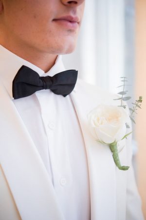 White groom tuxedo with black bow tie and white rose boutonnière - Elizabeth Nord Photography