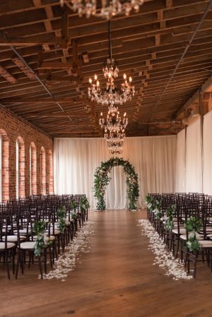 Indoor wedding ceremony decor with greenery arch - Photography by Marirosa