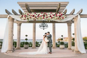 Bride and groom kissing under luxurious wedding pergola with flowers A Glamorous Wedding with Fireworks - Rachael Hall Photography