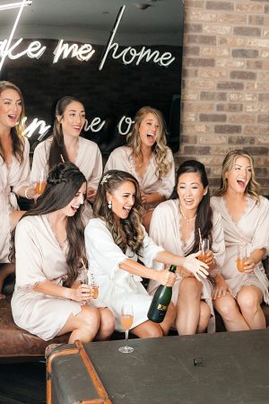 Bride and bridesmaids fun champagne popping photo - O’Malley Photography