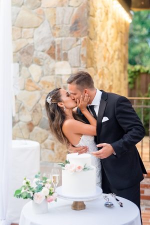 Bride and groom kiss at weeding cake table- O’Malley Photography