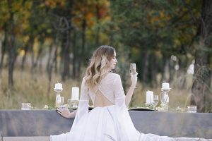 Bride at reception table with unique open back wedding dress - Photo: Tiffany Hudson Films