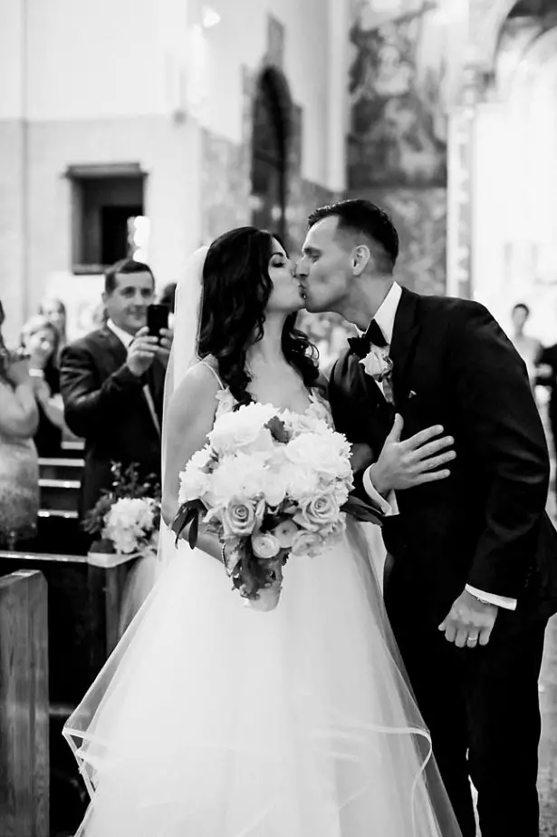 Church wedding recessional photo of bride and groom kissing - Bluespark Photography