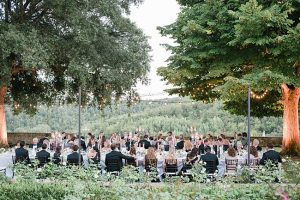 Perfect outdoor wedding reception in Tuscany with guests at tables under the trees and string lights - Purewhite Photography