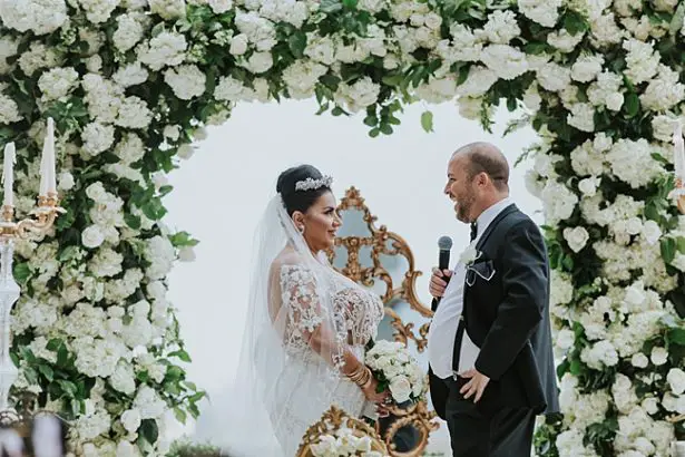 Bride and groom picture with white floral ceremony arch - Photo: Dmitry Shumanev Production