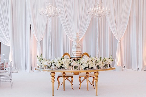 Gold Opulent Wedding reception sweetheart table decorated with chandeliers and white flowers - Photo: Dmitry Shumanev Production
